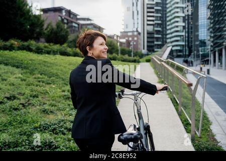 Lächelnde Geschäftsfrau mit Fahrrad zu Fuß in der Stadt Stockfoto