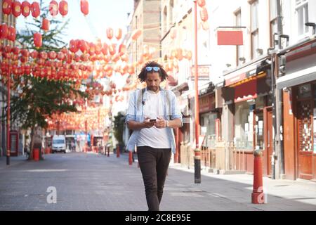 Junger Mann, der auf der Straße auf Smartphone schaut, Chinatown, London, Großbritannien Stockfoto