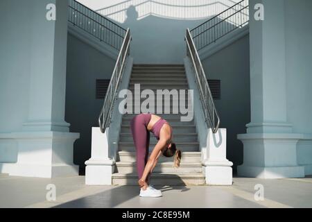 Junge Frau üben Vorwärtsbeuge Pose auf dem Boden durch Treppe Stockfoto