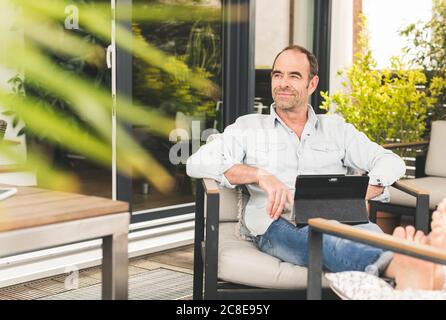 Durchdachte reife Geschäftsmann wegschauen, während mit digitalen Tablet sitzen Im Hinterhof Stockfoto