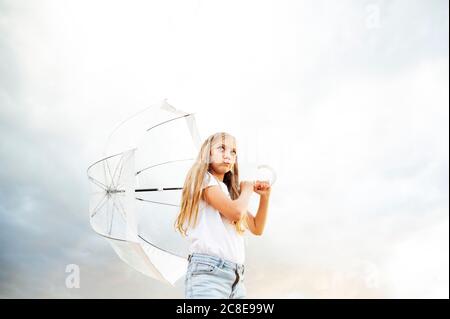 Blonde Mädchen macht Gesicht, während Regenschirm halten und wegschauen Es weht schwacher bewölktes Wetter Stockfoto