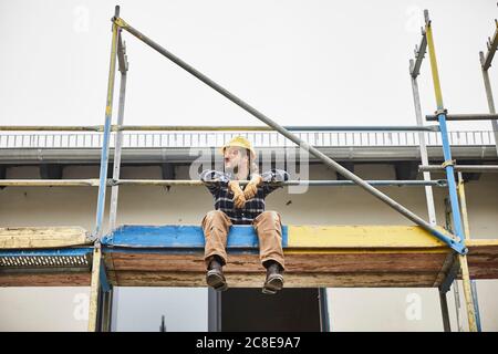 Arbeiter, der eine Pause hat, sitzt auf einem Gerüst auf einer Konstruktion Standort Stockfoto