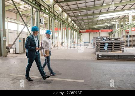 Zwei Geschäftsleute, die sich treffen und in einer Fabrik spazieren gehen Stockfoto