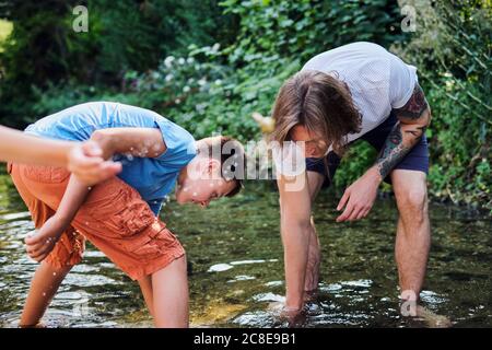 Mann, der mit dem Jungen im Bachwasser am Wald erkundet Stockfoto