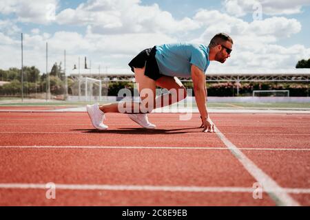 Männlicher Athlet in Startposition auf der Tartanbahn Stockfoto