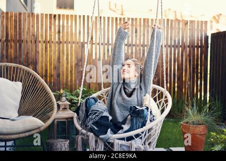 Glückliche junge Frau mit erhobenen Armen entspannen auf Schaukel in Hof Stockfoto