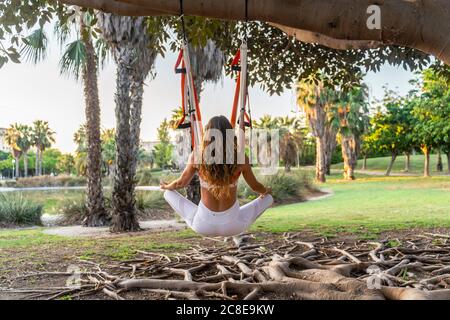 Reife Frau meditiert während sie im Park Aerial Yoga praktiziert Stockfoto
