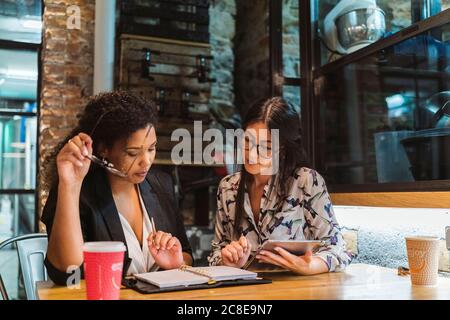 Multiethnische Kolleginnen diskutieren über digitale Tablets und Tagebuch, während Sitzen im Coffee Shop während des Meetings Stockfoto