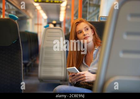 Nachdenkliche Frau hält Smartphone, während sie im Zug sitzt Stockfoto