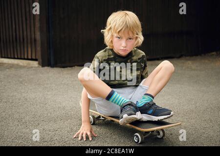 Netter Junge sitzt auf Skateboard auf dem Hof Stockfoto