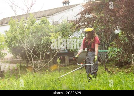 Mid adult Frau Schneiden Gras mit Benzin-Maschine auf dem Bauernhof Stockfoto