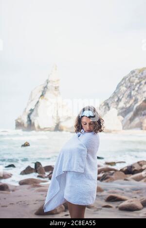 Junge Frau in Handtuch gewickelt, während sie am Strand von Ursa, Portugal, stand Stockfoto