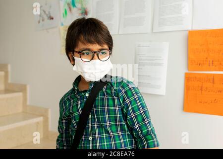 Junge mit Maske, der wegschaut, während er gegen die Wand steht Schule Stockfoto