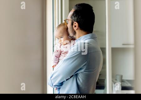 Vater mit Baby, der zu Hause aus dem Fenster schaut Stockfoto