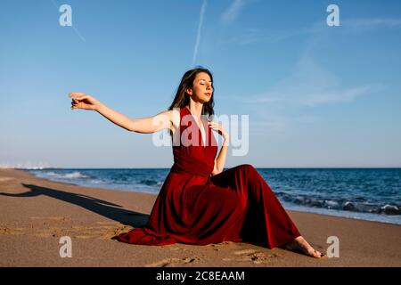 Zarte Frau in roten Kleid sittingh am Strand, das Gefühl der Sonne Stockfoto