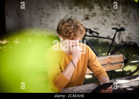 Junger Mann sitzt am Biertisch im Garten mit digitalen Tablet Stockfoto