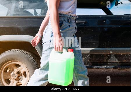 Mittelteil der Frau trägt Kühlmittel Gallone Behälter beim Gehen vorbei 4x4 Fahrzeug an sonnigen Tag Stockfoto