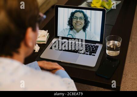 Lächelnder Arzt auf Videoanruf mit kranken älteren Frau durch Notebook Stockfoto