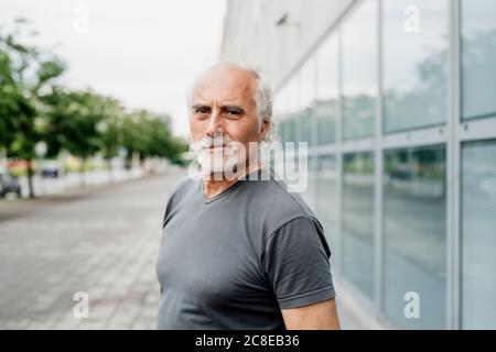 Selbstbewusster älterer Mann, der gegen Gebäude in der Stadt steht Stockfoto