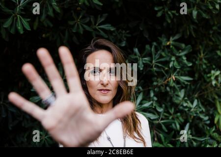 Schöne Frau zeigt Stop-Geste gegen Pflanzen im Park Stockfoto