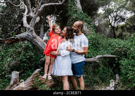 Eltern schauen auf die Tochter, die auf einem umgestürzten Baum im Wald steht Stockfoto