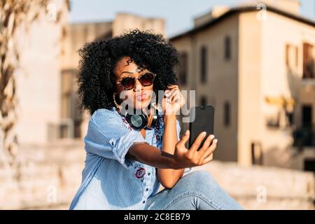 Lächelnde Frau mit Afro-Haaren und Sonnenbrillen, die ein Selfie machen Mit ihrem Smartphone Stockfoto