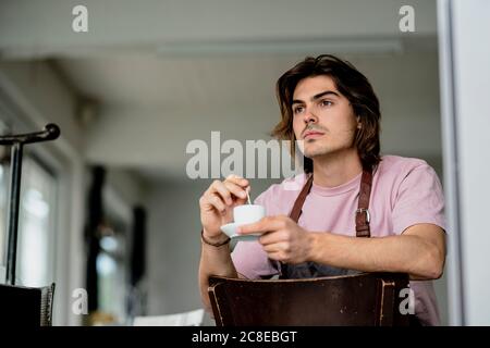 Durchdachter Besitzer hält Kaffeetasse, während er auf einem Stuhl sitzt Café Stockfoto