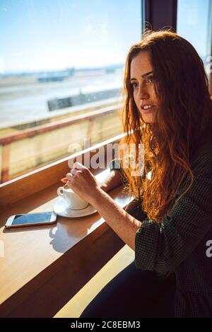 Durchdachte Geschäftsfrau, die Kaffee im Flughafencafe rührt Stockfoto