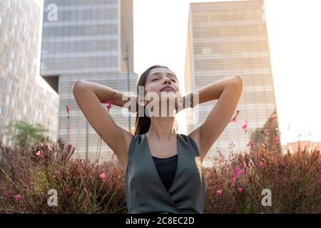 Entspannte junge Geschäftsfrau, die mit den Händen hinter dem Kopfhörer Musik hört Während der Pause gegen das Bürogebäude gehen Stockfoto