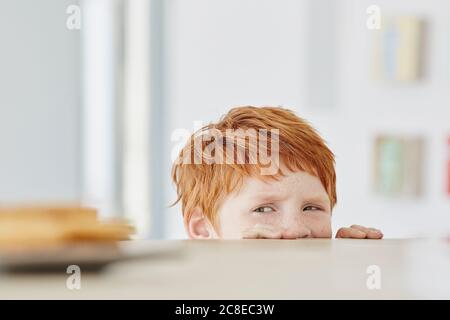 Porträt eines niedlichen Jungen zu Hause Blick auf Teller Auf dem Tisch Stockfoto