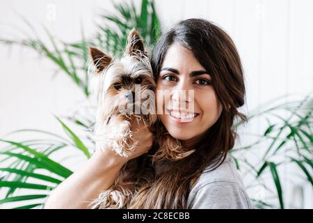Glückliche junge Frau, die Yorkshire Terrier zu Hause trägt Stockfoto