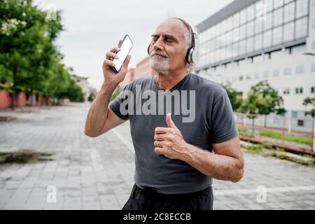 Ältere Frau mit geschlossenen Augen und Musik hören, während sie darauf steht Fußweg in der Stadt Stockfoto