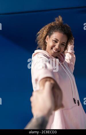 Lächelnde junge Frau trägt rosa Kapuzenpullover mit der Hand des Mannes Stockfoto