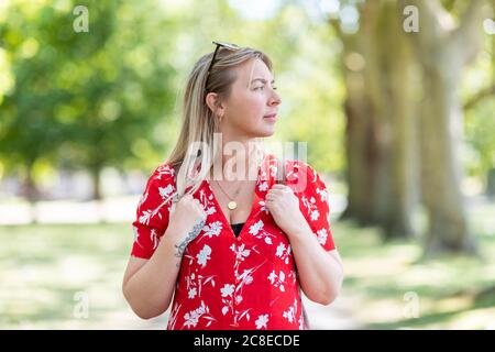 Nachdenkliche Frau, die an sonnigen Tagen im öffentlichen Park steht Stockfoto