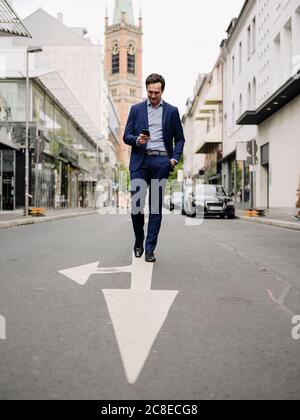 Reifer Geschäftsmann zu Fuß auf einer Stadtstraße mit Smartphone Stockfoto