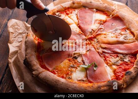 Frau Hand schneiden köstliche Pizza auf einem Holztisch Stockfoto