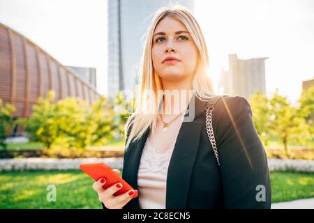 Nahaufnahme einer durchdachten Geschäftsfrau, die im Stehen ein Smartphone hält Stadt Stockfoto