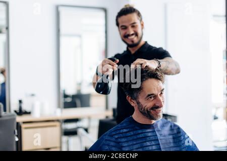 Glücklicher Friseur, der im Salon Wasser auf die Haare des Mannes sprüht Stockfoto