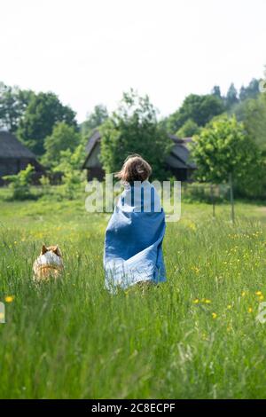 Junge mit Umhang, der mit Hund auf grasbewachsenem Land steht Der Himmel ist klar Stockfoto