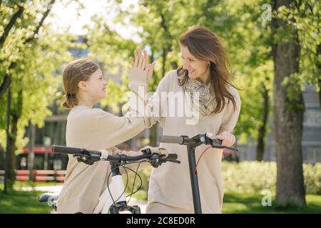 Glückliche Mutter und Tochter geben hohe fünf beim Stehen gegen Bäume im Stadtpark Stockfoto