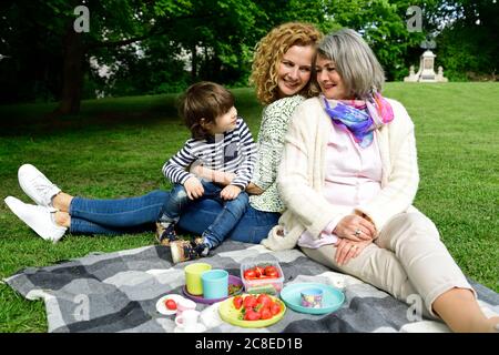 Happy boy enjoying picnic with mother and grandmother at public park Stockfoto