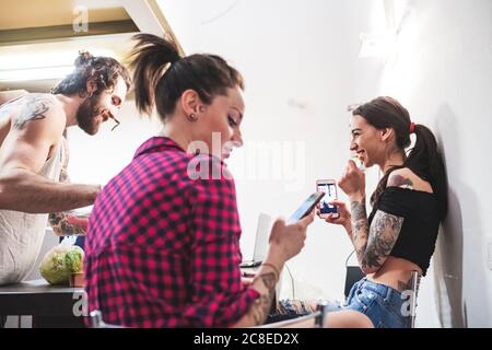 Frau mit Smartphone, während sie sich mit Mitbewohnern in der Party abkühlte Zu Hause Stockfoto