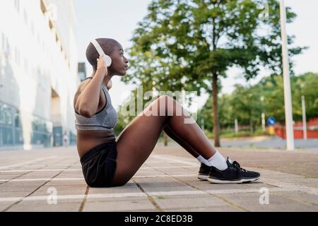 Junge Frau, die Musik hört, während sie auf dem Fußweg in der Stadt trainiert Stockfoto