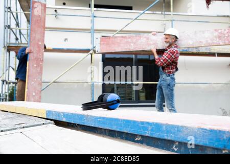 Ohrenschützer auf Holz mit männlichem Arbeiter, der Holz hereinträgt Hintergrund auf der Baustelle Stockfoto