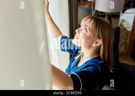 Nahaufnahme des Zimmermädchens, das die Vorhänge des Fensters im Hotelzimmer öffnete Stockfoto