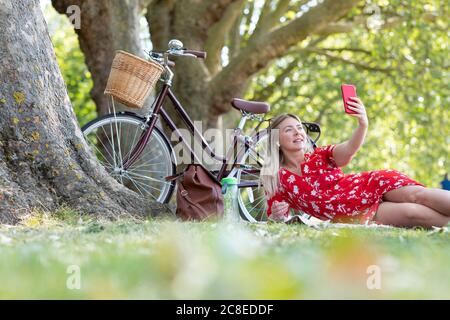 Frau, die Selfie über das Smartphone nimmt, während sie in der Öffentlichkeit liegt parken Stockfoto