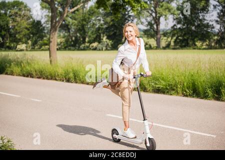 Spielerische Geschäftsfrau pendeln auf Elektro-Roller im Sommer Stockfoto