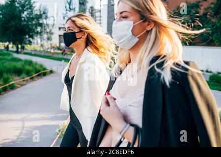 Weibliche Kollegen tragen Masken zu Fuß auf dem Weg in der Stadt Stockfoto