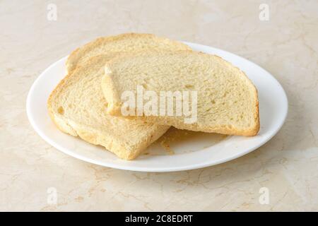 Wenige Scheiben Weizenbrot, getrocknet genug, um Brotbrösel auf einem weißen Teller über einem Küchentisch zu machen. Zutat für Fleischbällchen und Koteletts. Kochen Sie zu Hause. Stockfoto