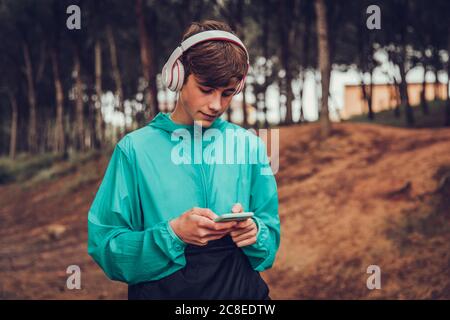 Teenager mit Kopfhörern im Regenmantel im Wald Stockfoto